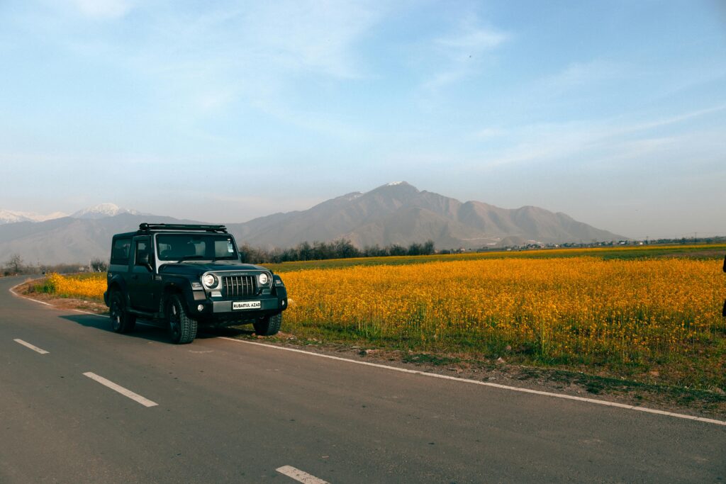 Mahindra Thar parked by a vibrant yellow field under a clear blue sky in Kashmir, India.